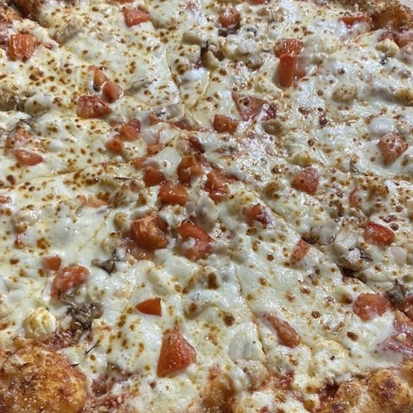 Close-up of a Mr Pizza pie, topped with melted cheese, diced tomatoes, and other toppings.